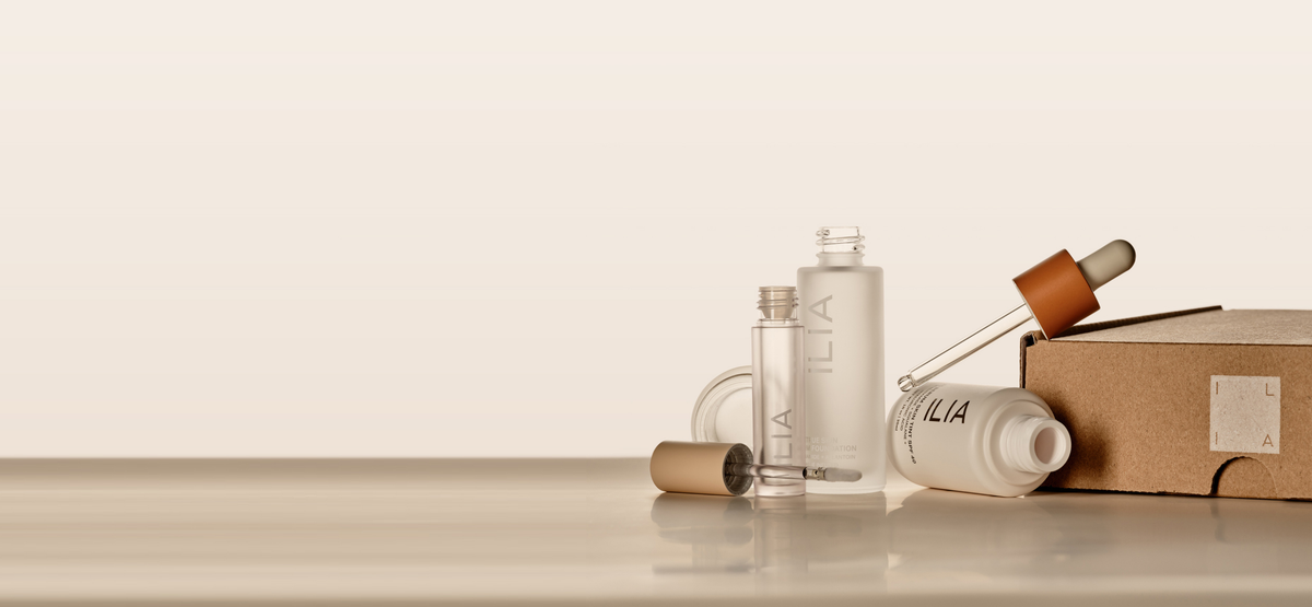 Minimalist, empty beauty products with ILIA branding, including serum and mascara, placed on a neutral surface.