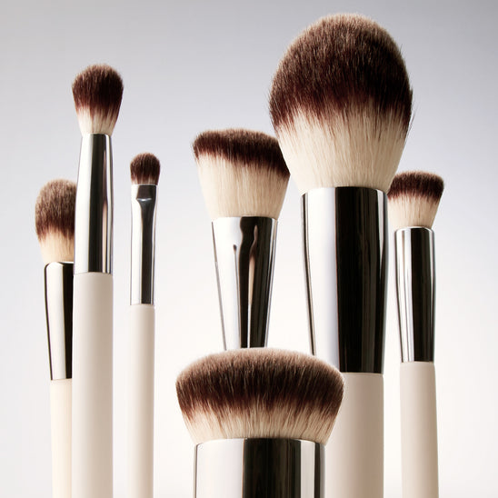 Set of ILIA makeup brushes with silver and black handles on a light gray background