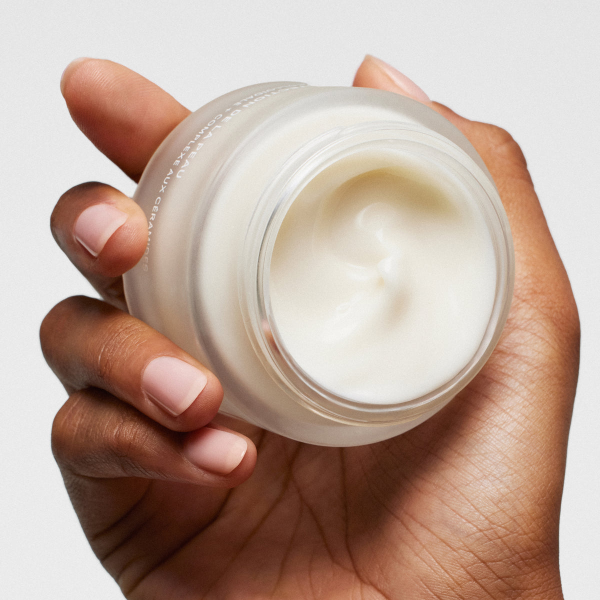 Hand holding a jar of ILIA's Barrier Build cream against a neutral background