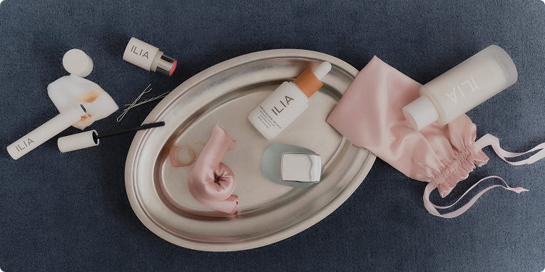 ILIA beauty products including skincare bottle and a pouch on a dark surface with 'ILIA' branding.